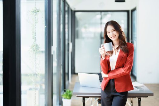 Portrait of a woman business owner showing a happy smiling face as he has successfully invested her business using computers and financial budget documents at work.