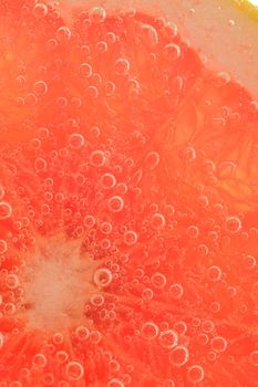 Close-up of a grapefruit slice in liquid with bubbles. Slice of red ripe grapefruit in water. Close-up of fresh grapefruit slice covered by bubbles.