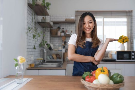 Portrait of young happy woman wearing appron standing in the kitchen room, prepares cooking healthy food from fresh vegetables and fruits...