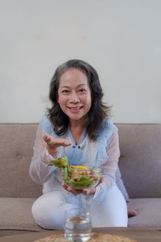 Happy old asian woman eating fresh green salad. Senior woman good healthy at home. Exercise and healthy diet concept.