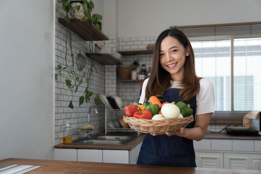 Portrait of young happy woman wearing appron standing in the kitchen room, prepares cooking healthy food from fresh vegetables and fruits...