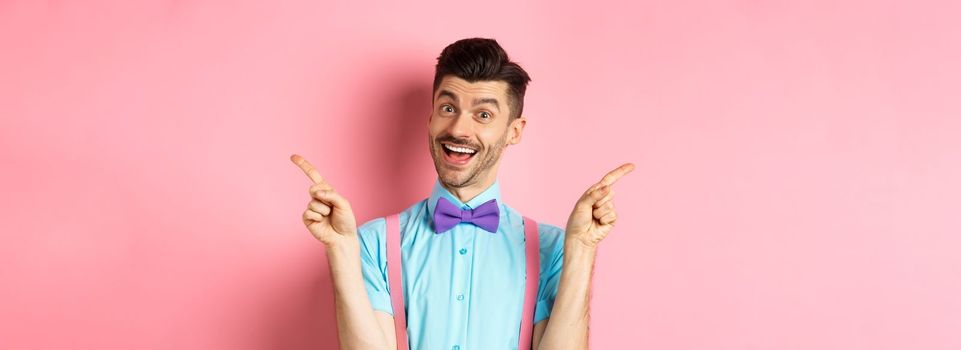 Handsome funny guy pointing fingers aside, showing left and right logo and smiling, recommending two choices, standing on pink background.