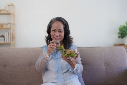 Happy old asian woman eating fresh green salad. Senior woman good healthy at home. Exercise and healthy diet concept.