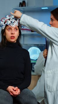 Doctor researcher adjusting EEG headset analyzing patient's evolution after treatment against disease of nervous system. Team of scientists working late night in neurological research laboratory