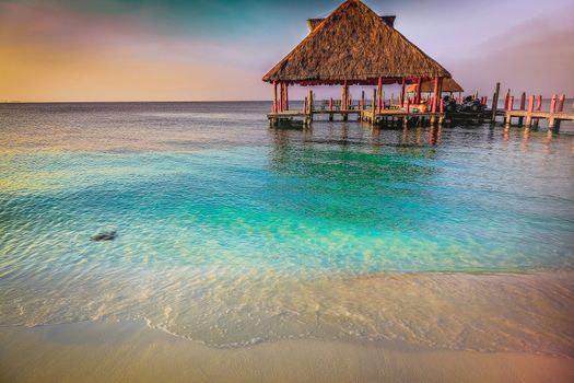 Tropical paradise, sand beach in caribbean with palapa and pier at sunset, Cancun, Mexico