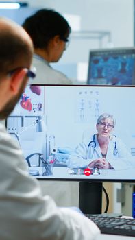 Senior woman doctor offering medical online advices to chemist using pc webcam. Scientist holding blood sample during online discussion, virtual conference, helping on telemedicine, healthcare support