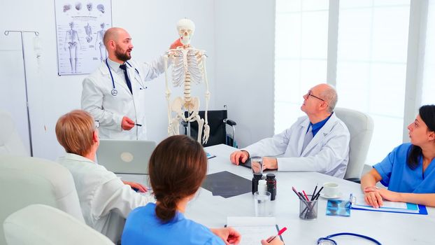 Expert radiologist demonstrating on skeleton during briefing with medical staff in hospital meeting room. Clinic therapist talking with colleagues about disease, medicine professional