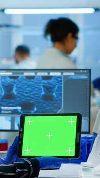 Medical research scientist working on tablet with green screen mock up template in applied science lab. Engineers conducting experiments in background, examining vaccine evolution using high tech