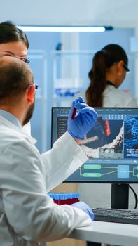 Group of scientists working in modern equipped laboratory pointing on computer desktop. Team of doctors examining vaccine evolution using high tech researching diagnosis against covid19 virus