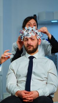 Neurological researchers explaning treatment result pointing on monitor while medical scientist adjusting brainwave scanning headset preparing for brain scan analysing electrical activity