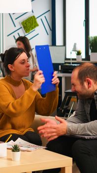 Angry manager woman screaming at diverse employees disagreeing about bad business contract, hitting man with clipboard in head sitting on couch at office desk, conflict dispute about document