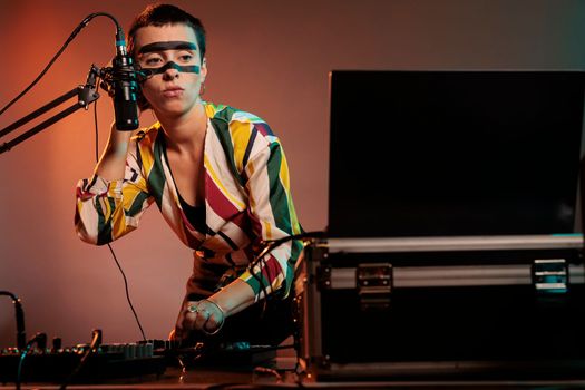 Female performer producing techno music at mixer, having crazy make up and playing with audio stereo equipment. Musician artist mixing sounds at turntables to make musical performance in studio.