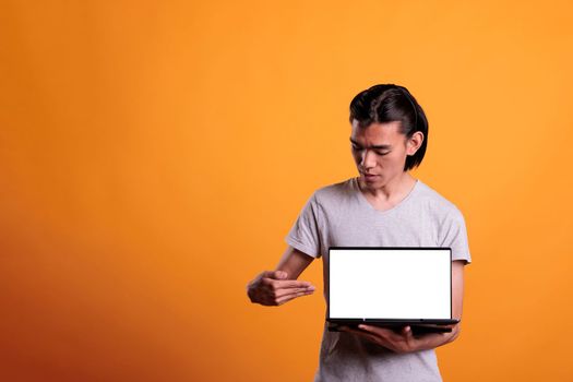 Confident asian man pointing at laptop with white blank screen, software advertising mockup with place for text. Attractive serious person presenting portable computer with empty display