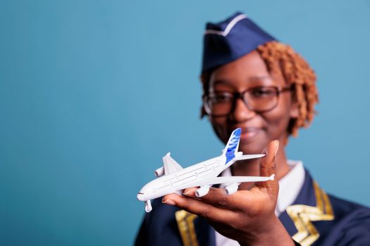 Aircraft attendant in crew uniform looking at model airplane, holding it in his hands with a smile. Female professional flight assistant with commercial toy airplane in studio shot.