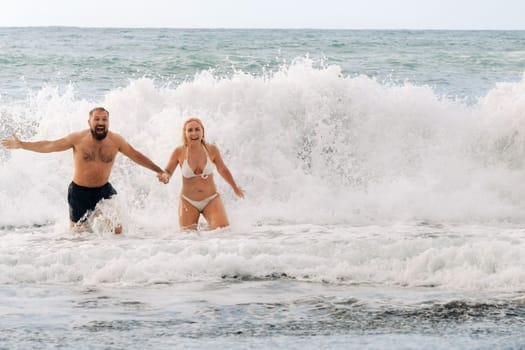 A married couple swims in the sea on the waves, holding hands. The concept of a romantic trip.