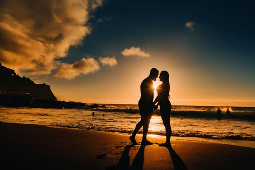 A couple in love is standing on the beach holding hands at sunset. The concept of a romantic trip.