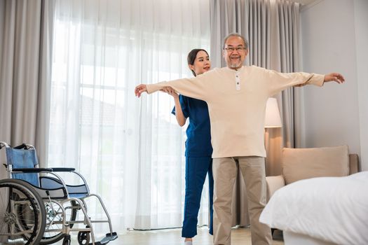 Rehabilitation of disabled people. Old senior man enjoys training with physiotherapist for outstretched arms at home, Asian physical therapist patient help elderly exercising arm stretch