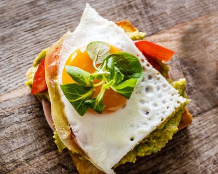 Toasted bread with egg, tomato and spinach for healthy protein breakfast on wooden table. Tasty morning sandwich for fast diet and nutrition