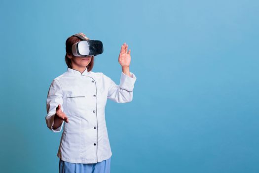 Positive senior cook wearing virtual reality goggles while preparing culinary meal working at healthy recipe. Friendly chef with restaurant uniform cooking gastronomy food dish. Food industry
