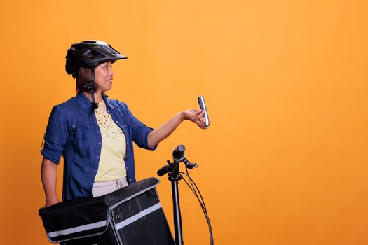 Restaurant employee with blue uniform and helmet delivering fast food order giving POS terminal to customer. Pizzeria employee using bike as transportation while carrying takeout food backpack