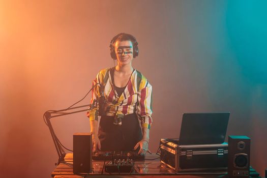 Cool artist mixing tunes at turntables, using dj audio instrument and equipment to play techno music. Happy woman with crazy make up using electronics to do musical performance.