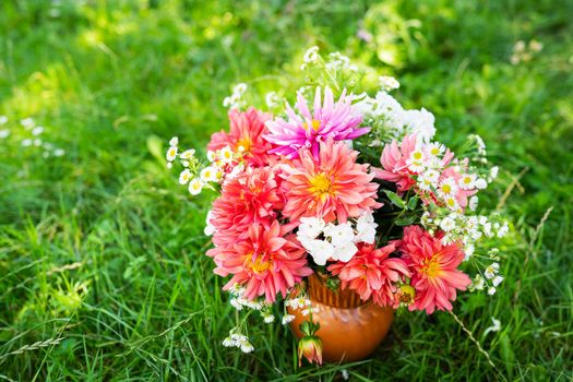 A bright colorful bouquet of garden and wild fresh flowers that stands in a vase on the grass. Very colorful and bright bouquet, place for an inscription