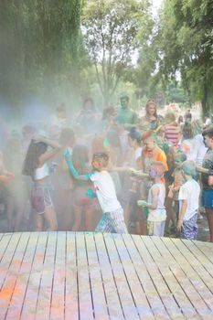 Lviv, Ukraine - July 18, 2021: Color Holi Festival, a crowd of people adults and small children throw colorful paint. Indian holiday, children running on a wooden stage