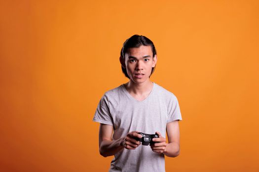 Young asian man playing computer video games with joystick, entertainment activity, fun pastime. Concentrated teenager holding console wireless controller, enjoying videogames