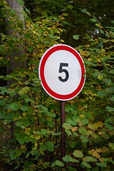 A sign indicating a speed limit of five miles per hour is in the park, in the forest