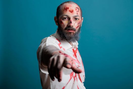 Portrait of halloween zombie posing on camera, looking spooky and dangerous with apocalyptic scars and bloody wounds in studio. Evil aggressive brain eating monster, frightening corpse.