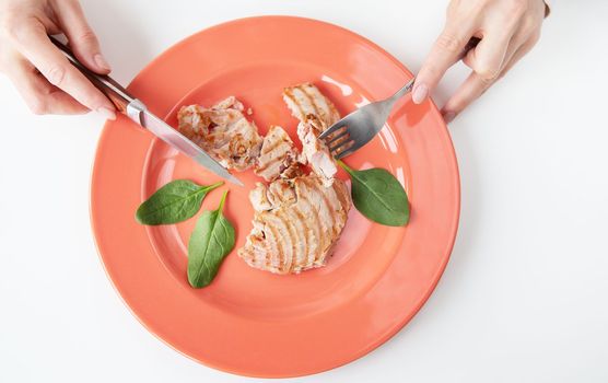 Close-up shot of a juicy delicious grilled tuna steak on a bright coral plate. Delicious and healthy food, proper nutrition. The girl is holding a fork and knife. View from above