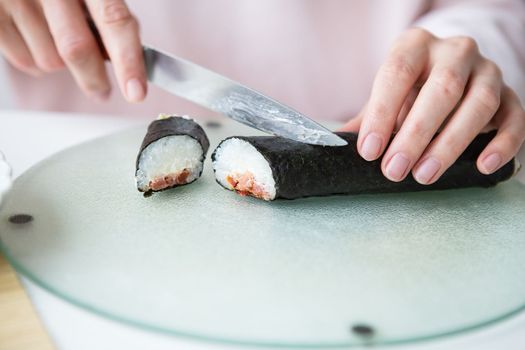 The process of making sushi, the girl makes sushi with different flavors - fresh salmon, caviar, avocado, cucumber, ginger, rice. Cut the roll into pieces. Close-up