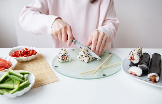 The process of making sushi, the girl makes sushi with different flavors - fresh salmon, caviar, avocado, cucumber, ginger, rice. Cut the roll into pieces