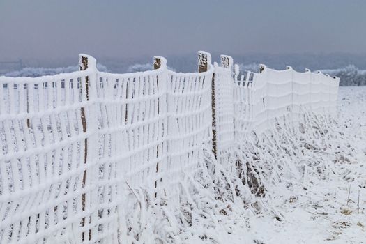 A fence white with snow in a rural area in cold winter, Germany