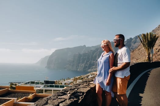 A couple in love stands on an observation deck against the backdrop of the Acantilados de Los Gigantes mountains at sunset, Tenerife, Canary Islands, Spain.