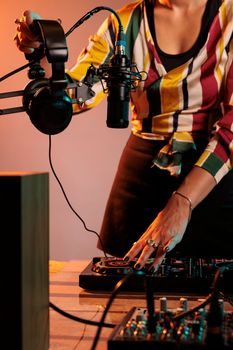 Woman musician using dj equipment and headphones to mix techno music and play electric remix on turntables, having fun with stereo instrument used for mixing sounds, bass volume.