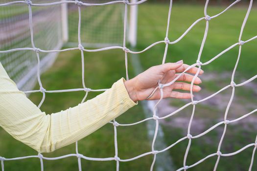 A girl stands near a white net close-up on a soccer field, a soccer goal. Green field