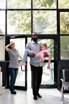 Scared dad walking in hospital waiting area holding fainted unconscious daughter in arms trying to get help from doctor. Caucasian little child faints and collapses. Health care service and concept