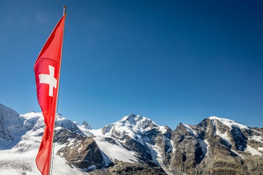 Swiss flag and Bernina mountain range with glaciers in the Alps, Engadine, Switzerland