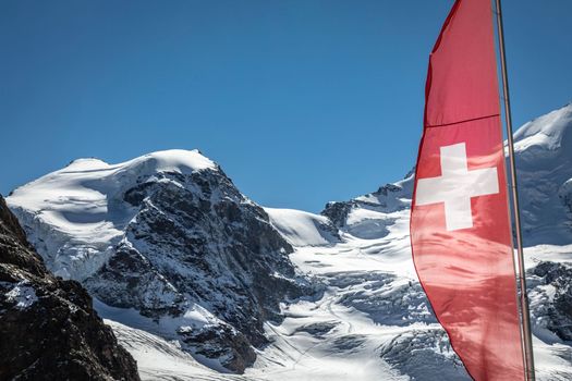 Swiss flag and Bernina mountain range with glaciers in the Alps, Engadine, Switzerland