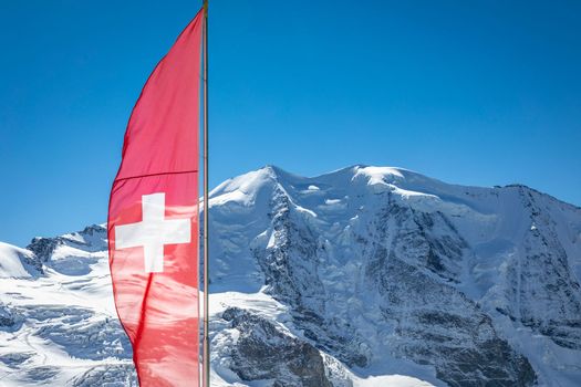 Swiss flag and Bernina mountain range with glaciers in the Alps, Engadine, Switzerland