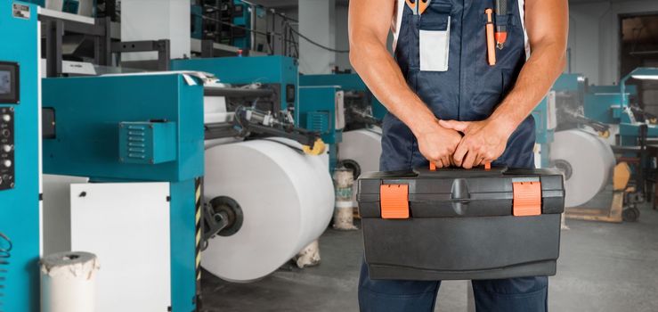 Man with tool box working in printing house with an printing machine