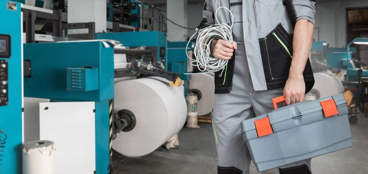 Man with tool box working in printing house with an printing machine