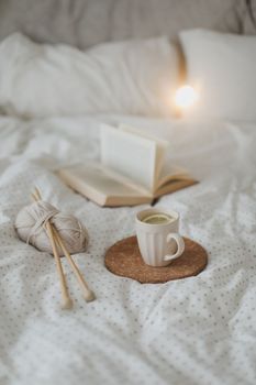 Cozy winter background with a book, tea cup and knitting needles in warm soft bed top view