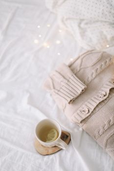Knitted beige sweater and cup of tea on messy bed background. Winter and spring fashion concept. Top view flat lay