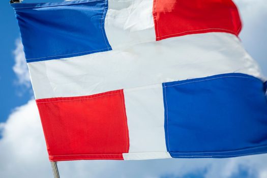 Dominican Republic National Flag Waving on pole against sunny blue sky in Punta Cana