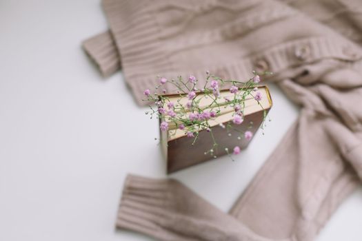 Warm knitted beige sweater and a book with flowers at white background. Cozy vintage. Flat lay, top view 