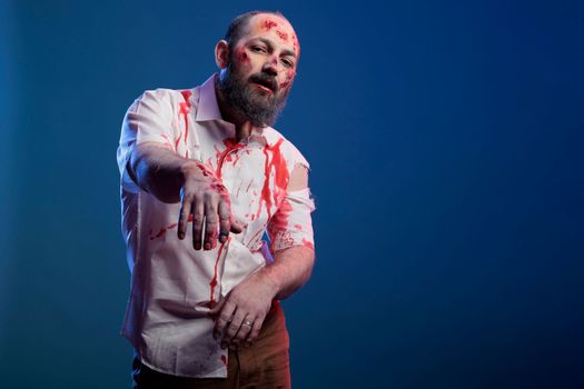 Halloween cruel zombie with bloody wounds, eating brain and looking dangerous over blue background. Spooky deadly monster with horror face and creepy evil corpse eyes, eerie villain.