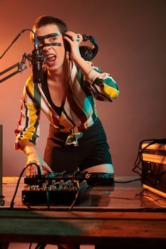 Musical performer mixing music at dj turntables, playing techno sounds with mixer and bass key in studio. Using headphones and microphone to create cool club performance, having crazy make up.