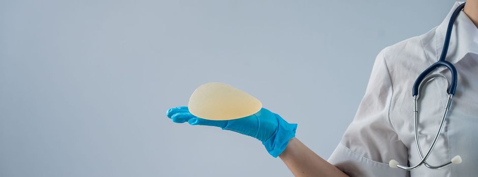 Female doctor aesthetic surgeon holding a breast implant on a white background